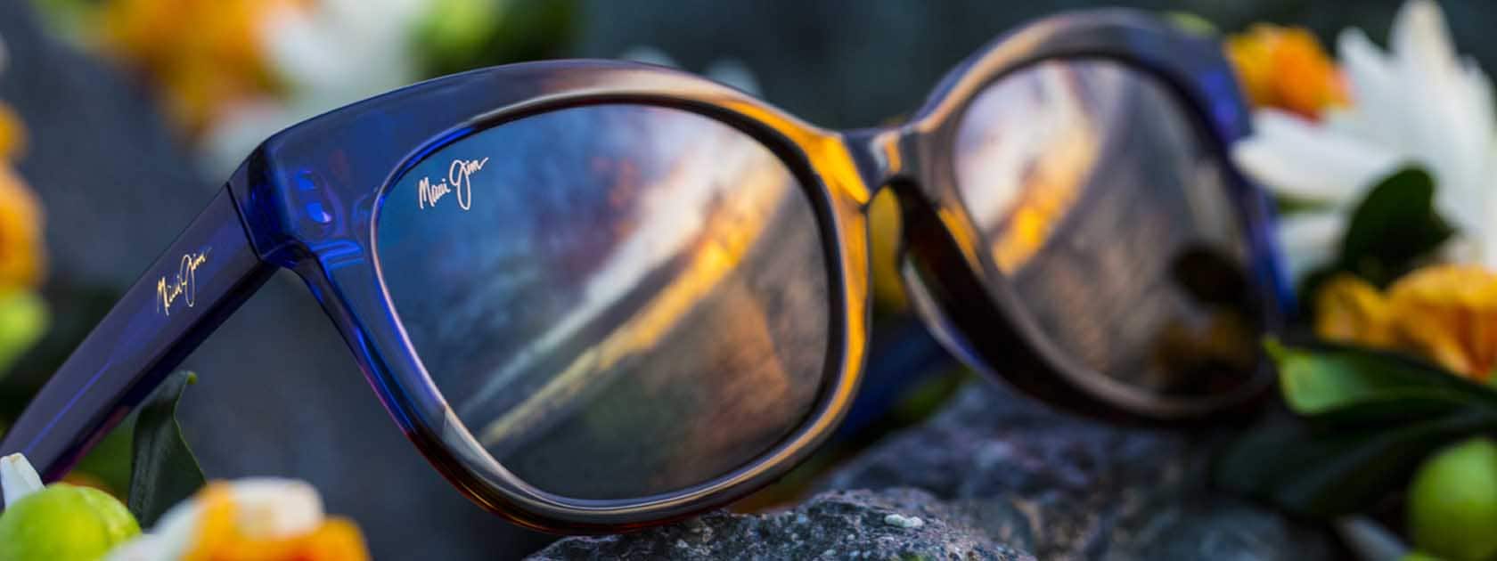 gafas de sol con el cielo reflejado en las lentes, expuestas sobre roca con flores blancas y amarillas y verdes
