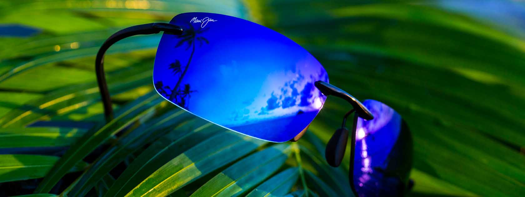frameless sunglasses with blue lenses displayed on palm leaves