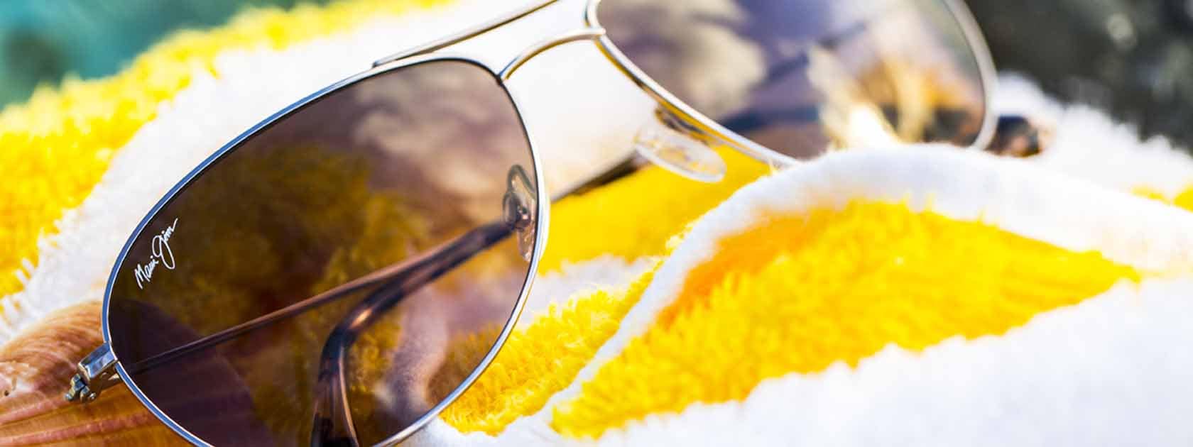 lunettes de soleil aviateur à la monture argentée avec verres gris présentées sur serviette rayée jaune et blanche