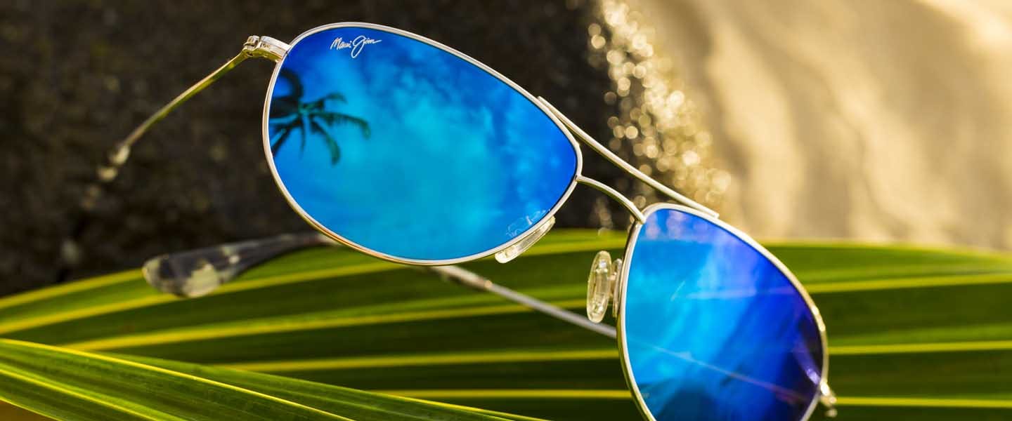 occhiali da sole baby beach in argento con lenti blu su foglie di palma