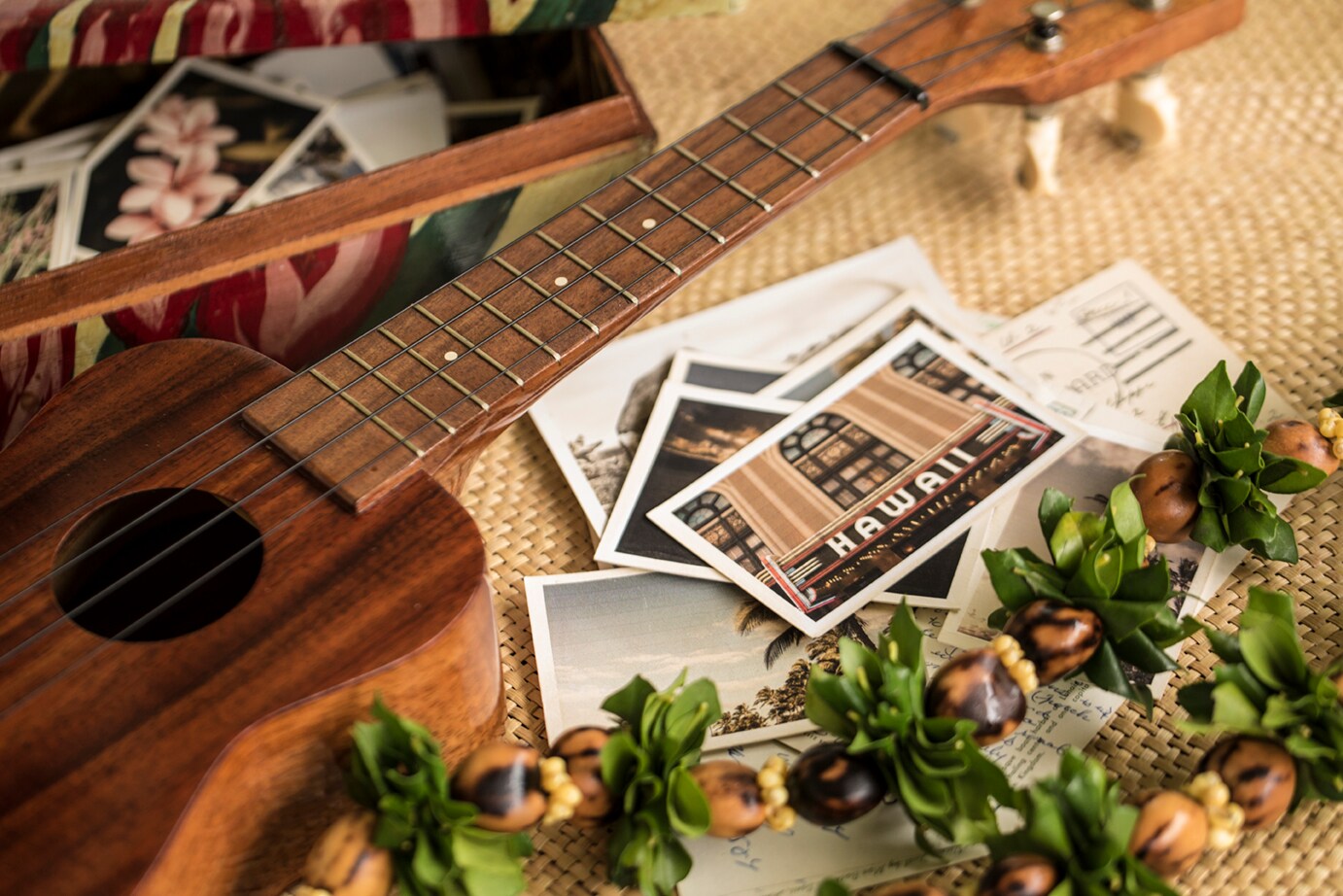 ukulele présenté sur un tapis de paille avec lei et cartes postales d'Hawaï