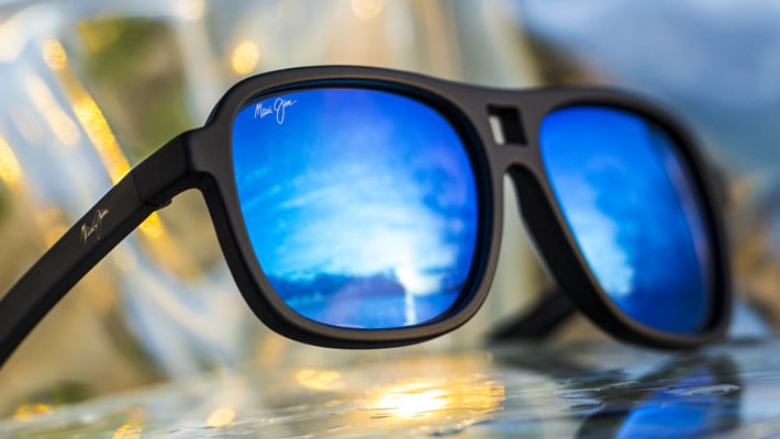 occhiali da sole con montatura nera opaca e lenti blu mostrati su una pietra