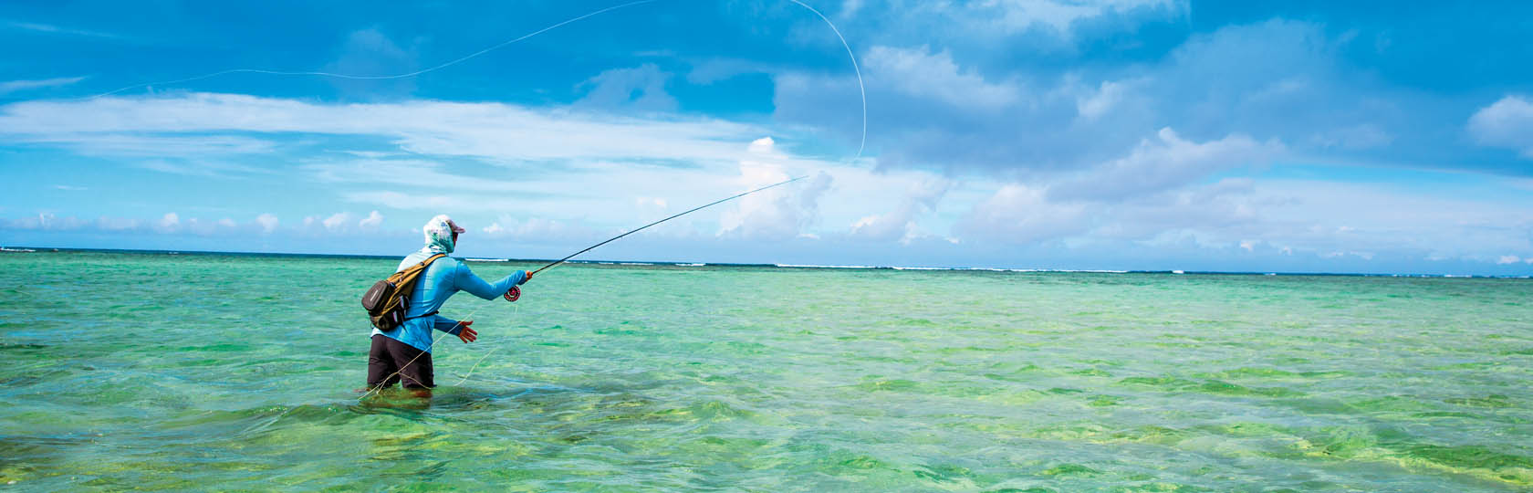 hombre con mochila pescando con el agua a las rodillas, con olas en la distancia