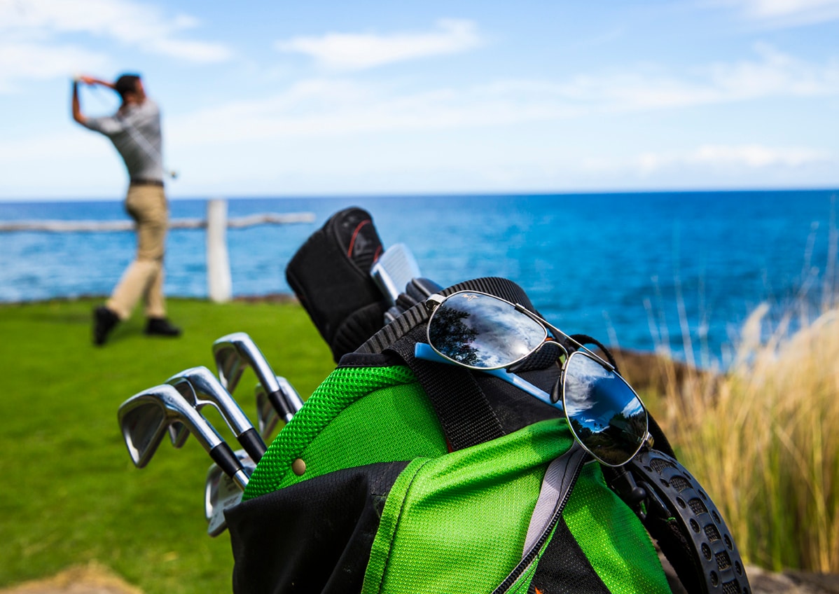 lentes de sol exhibidos colgados de una bolsa de golf verde con jugador de golf en el fondo golpeando la pelota