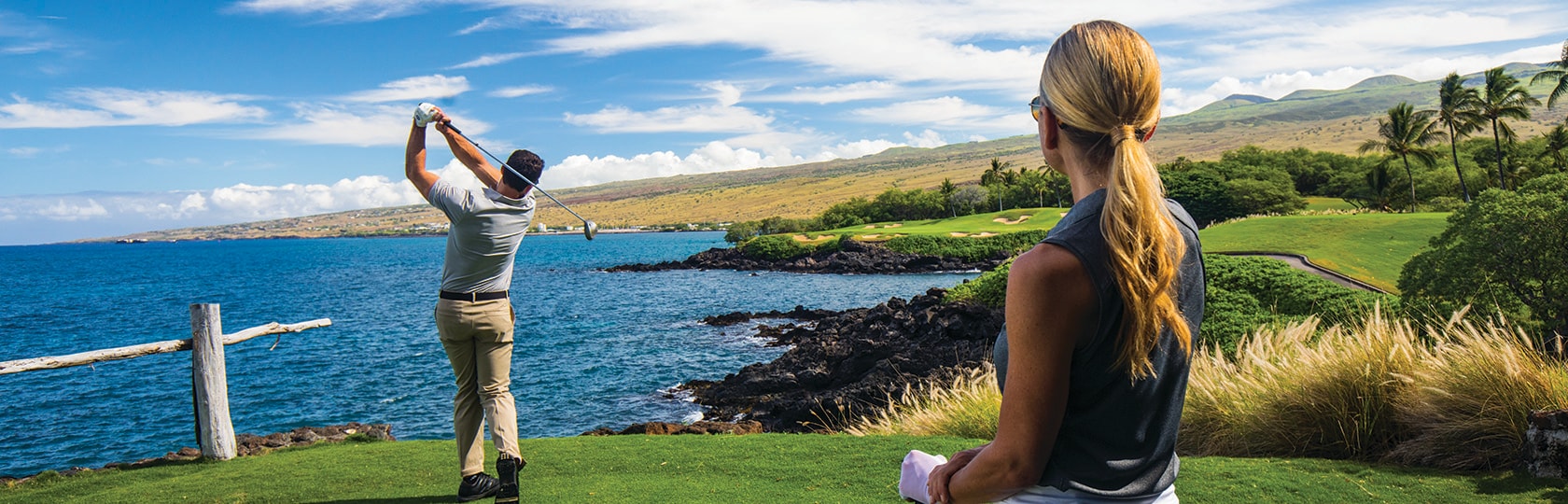 Mann, der einen Golfball auf einem Golfplatz am Meer abschlägt und von einer Frau beobachtet wird