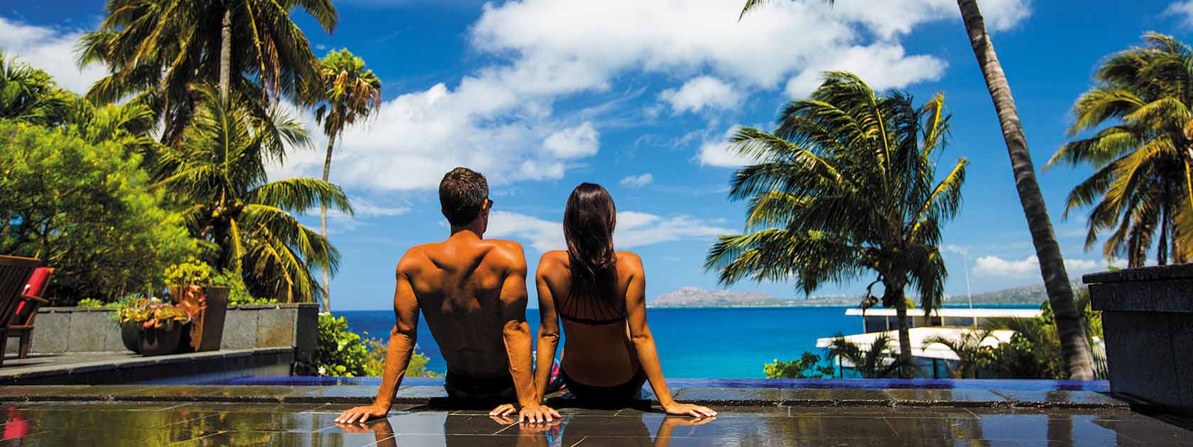 man and woman sitting poolside looking at the ocean in the distance