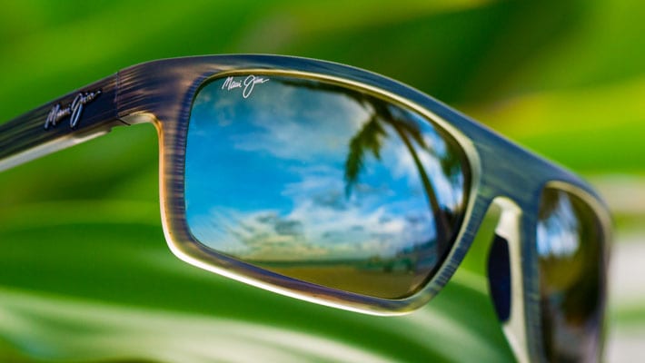 occhiali da sole con riflessi di palme sulle lenti e una foglia di palma verde come sfondo