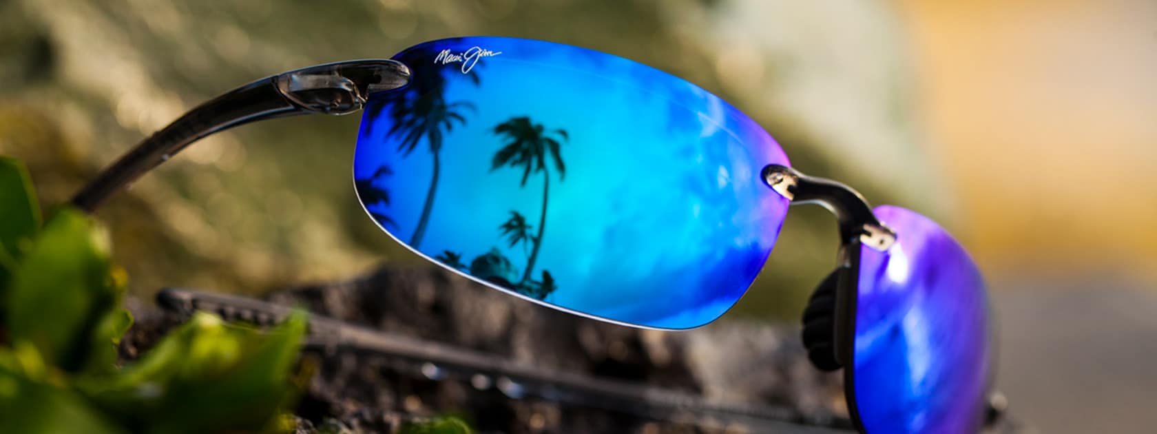 Sonnenbrille mit rauchgrauer Fassung und blauen Gläsern, in denen sich Palmen spiegeln