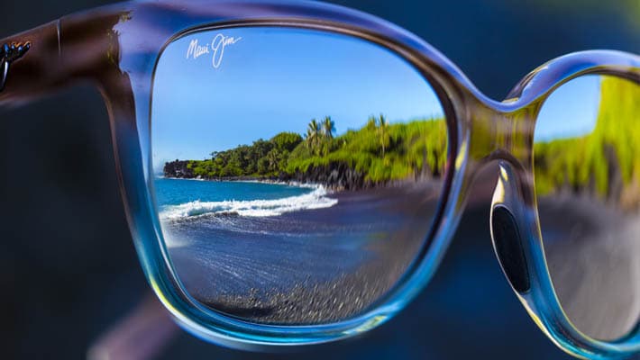 primo piano su lenti di occhiali da sole che riflettono l'immagine di una spiaggia colorata sull'oceano con palme