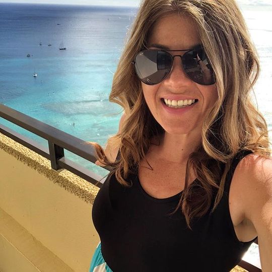 woman wearing black shirt and sunglasses standing at balcony overlooking ocean taking selfie