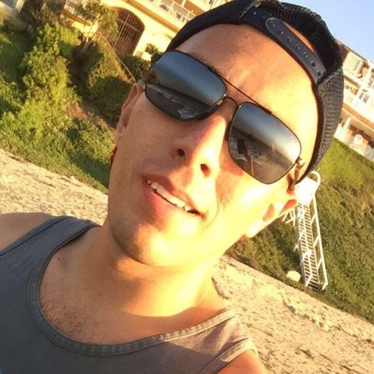 Mann mit Sonnenbrille und nach hinten gedrehter Kappe, der am Strand ein Selfie aufnimmt