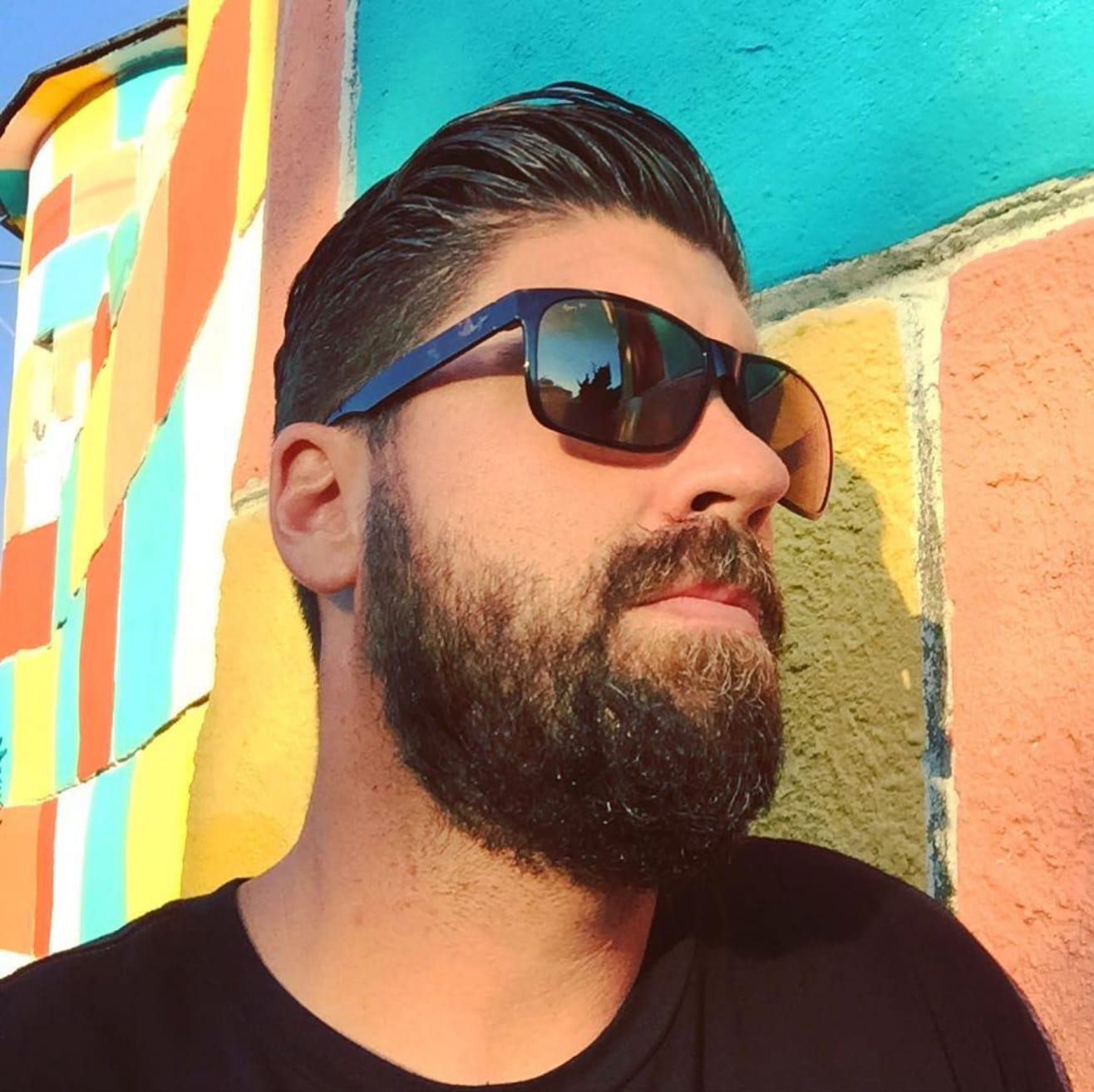 bearded man wearing sunglasses posing in front of a painted mural covered wall