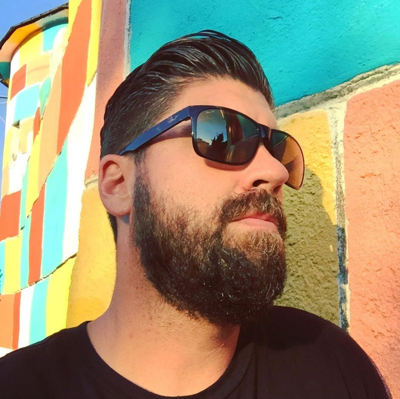 bearded man wearing sunglasses posing in front of a painted mural covered wall