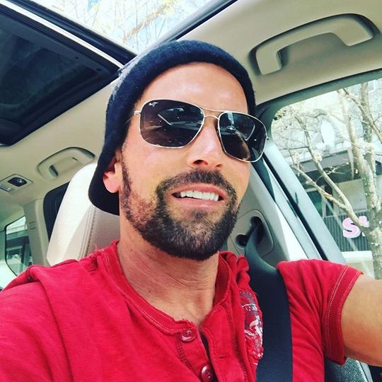 Mann mit rotem Shirt und Sonnenbrille in einem Auto, der ein Selfie aufnimmt