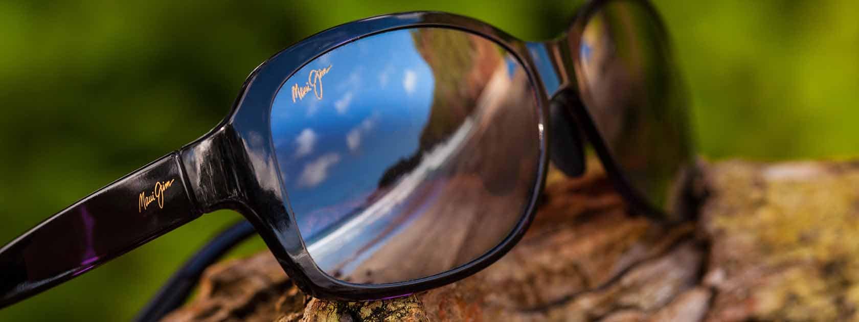 lunettes de soleil à monture noire avec reflet du ciel dans les verres présentées sur du bois