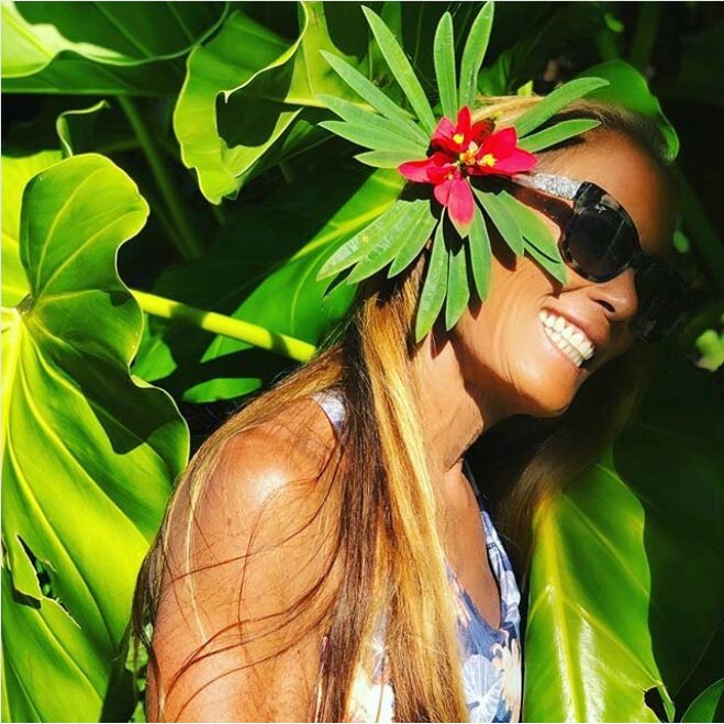 donna con fiore nei capelli in piedi accanto a grandi foglie tropicali verdi