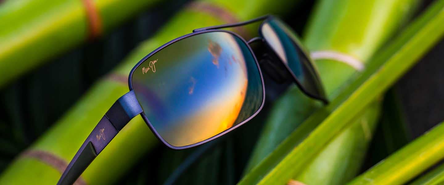 occhiali da sole con montatura metallica e lenti color bronzo mostrati su del bambù