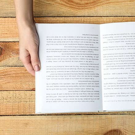 mains d'une personne tenant un livre sur une table en bois