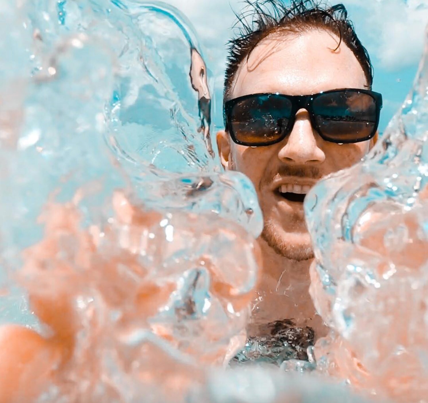 man wearing sunglasses taking a selfie being overtaken by a wave