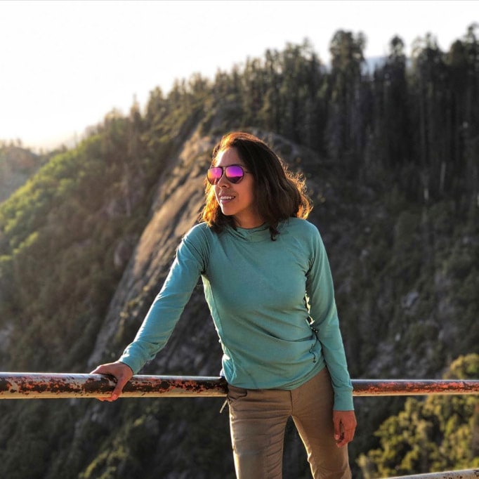 Woman wearing MAUI Sunrise Shallows, leaning against a rail with a mountain backdrop behind