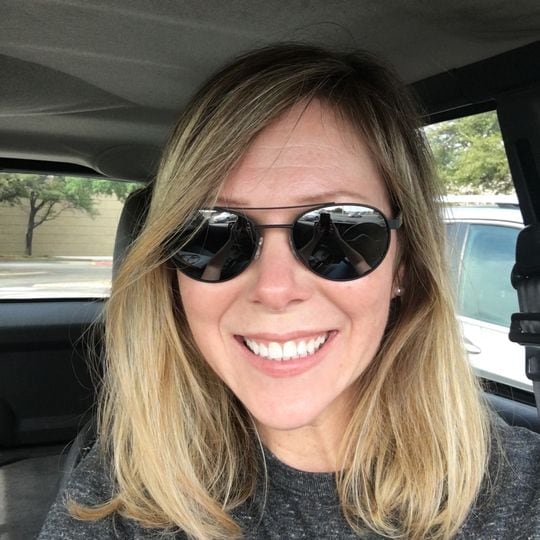 woman wearing gray shirt and sunglasses taking selfie in her car