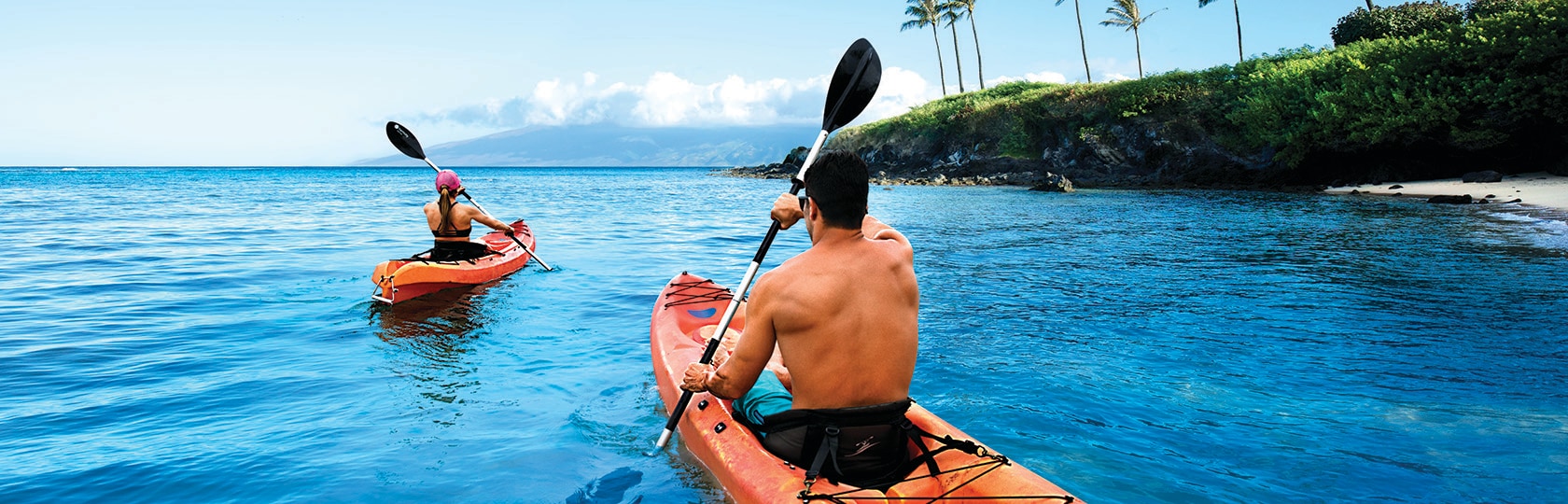 two people kayaking along side the ocean shore with palm trees